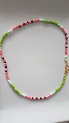 a necklace made with multicolored beads and a gold charm on a white surface