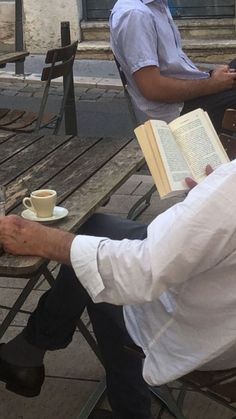 two men are sitting at an outdoor table with books and coffee in front of them