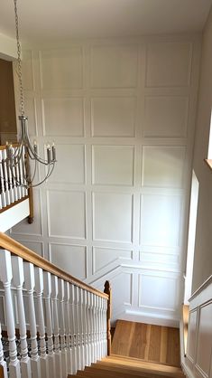 an empty staircase leading up to the second floor with white walls and wood floors, in front of a chandelier