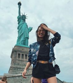 a woman standing in front of the statue of liberty