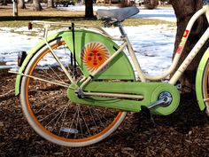 an orange and green bicycle parked next to a tree in front of snow covered ground