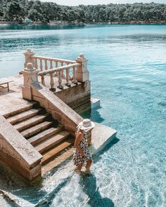 a woman standing in the water next to steps leading up to an outdoor swimming pool