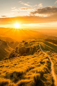 the sun is setting on top of a grassy hill with a trail going through it