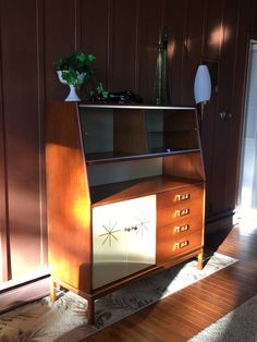 a wooden cabinet sitting on top of a hard wood floor next to a vase filled with flowers