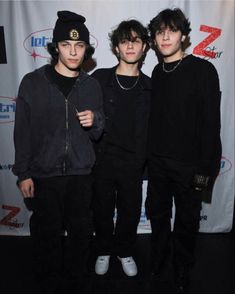 three young men standing next to each other in front of a red carpeted wall