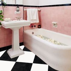 a bathroom with black and white checkered flooring, pink walls and bathtub