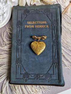 a book with a gold heart charm on it sitting next to some flowers and feathers