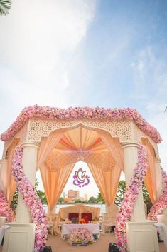 an outdoor wedding setup with pink flowers on the altar and white pillars, surrounded by palm trees