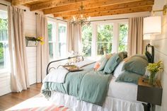 a large bed sitting inside of a bedroom next to a window covered in curtains and pillows