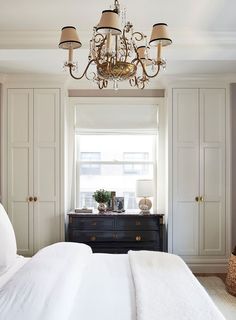 a chandelier hangs from the ceiling above a bed in a bedroom with white walls