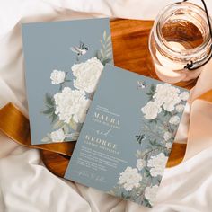 two blue and white wedding cards on top of a bed next to a jar of honey