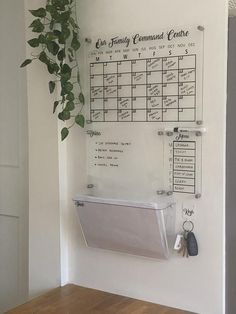 a wall mounted calendar on the side of a white wall next to a potted plant