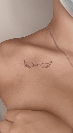 the back of a woman's chest with an angel wing tattoo on her left side