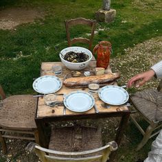 a woman sitting at a wooden table with plates and bowls on it, next to a bowl of food