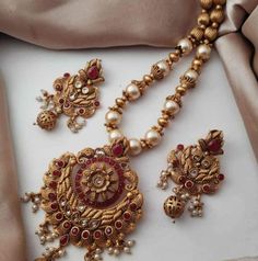 This beautiful Indian mala set features high-quality freshwater pearls and small, polished red gemstones, such as rubies or garnets, all elegantly set in a golden base. The necklace's traditional design showcases a symmetrical pattern of pearls interspersed with gemstones, enhanced by the golden setting and a central pendant. Matching earrings and a coordinated bracelet complete the set, echoing the necklace's luxurious style. Handcrafted by skilled artisans, the set combines premium materials a Elegant Kundan Jewelry Sets For Puja, Pearl Kundan Necklace With Intricate Design As A Gift, Festive Jewelry Sets With Pearl Pendant For Celebration, Traditional Pearl Bridal Necklace For Anniversary, Traditional Pearl Jewelry Sets, Elegant Hand Set Jewelry For Puja, Elegant Red Bridal Necklace For Puja, Elegant Round Kundan Necklace For Puja, Traditional Pearl Necklaces For Anniversary