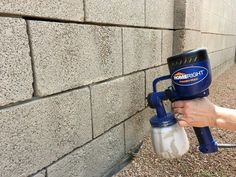 a person using a paint sprayer on a brick wall with a cement block in the background