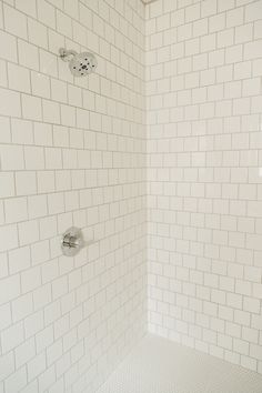 a white tiled shower stall with hand held shower head