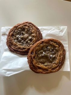 two chocolate chip cookies sitting on top of white paper