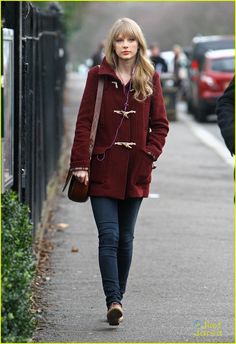 a woman is walking down the sidewalk with her handbag in her other hand and wearing a red coat