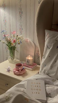 a book on a bed next to a vase with flowers and a lit candle in it