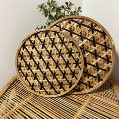 two round bamboo trays sitting on top of a wicker table next to a potted plant