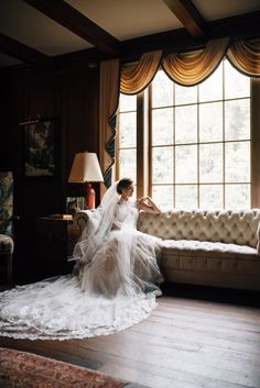 a woman in a wedding dress is sitting on a couch with her veil flowing over her head