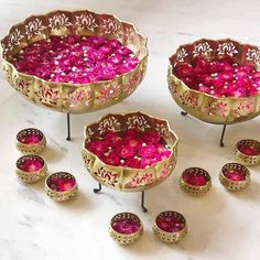 several metal bowls filled with pink flowers on top of a white countertop next to candles