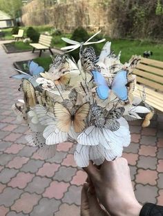 a person holding a bouquet of flowers with butterflies on it in front of a park bench