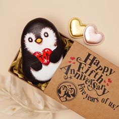 a penguin figurine sitting in a box next to two hearts