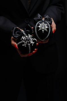 the woman is holding two black purses with bows on their hands, both decorated with jewels