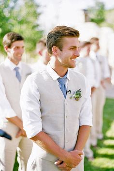 a man in a white suit and tie standing next to other men