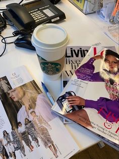 magazines, coffee cup and cell phone sitting on a desk with various fashion items in front of it