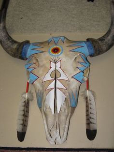 an animal skull with long horns and painted designs on it's face is hanging from the wall