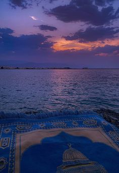 the sun is setting over an ocean with a rug on it