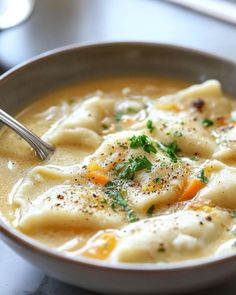 a white bowl filled with dumplings and carrots on top of a wooden table