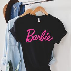 two shirts that say barbie on them hanging from a clothes rack next to a denim jacket