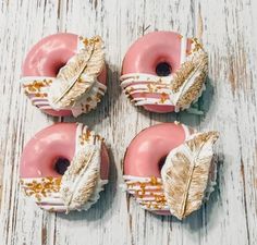 four doughnuts with pink frosting and gold leaf decorations on white wooden surface