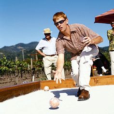 a man is bowling on the sand in front of other men