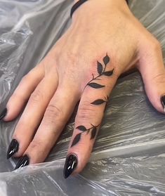 a woman's hand with black nail polishes on it and a leaf tattoo