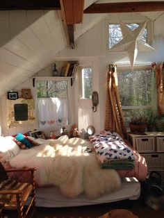 a bedroom with white walls and wooden floors has a large bed in the corner, along with two windows that look out onto the woods