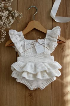 a white knitted romper with ruffles on it and a wooden hanger