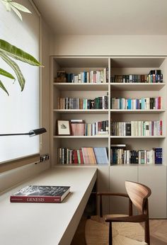 a book shelf filled with lots of books next to a chair and table in front of a window