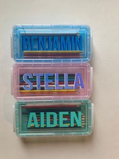 three plastic containers with name stickers in them on a white surface and one has the word steiela written on it