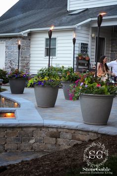 two people sitting at a table in front of a house with flowers on the patio