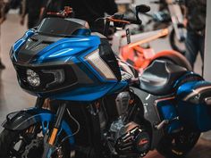 a blue and black motorcycle parked next to other motorcycles in a room with people standing around