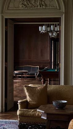 a living room filled with furniture and a chandelier hanging from the ceiling next to a pool table