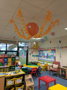 a classroom filled with lots of colorful tables and chairs next to a giant spider hanging from the ceiling