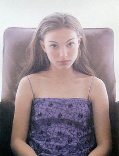 a young woman sitting in a chair with her hands on her knees looking at the camera