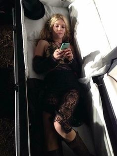 a woman laying in bed looking at her cell phone while wearing black stockings and boots