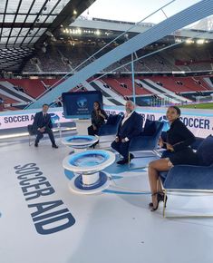 three people sitting in chairs on a stage at a soccer game, with one person speaking to the audience